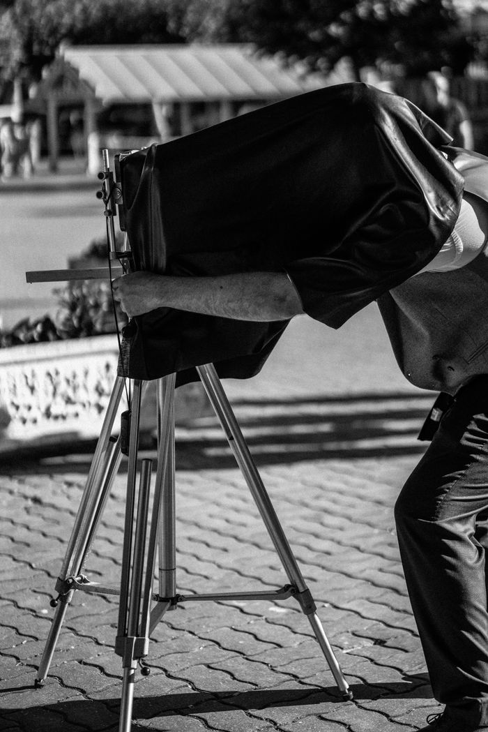 Black and white photo of a vintage photographer using a large format camera outdoors.